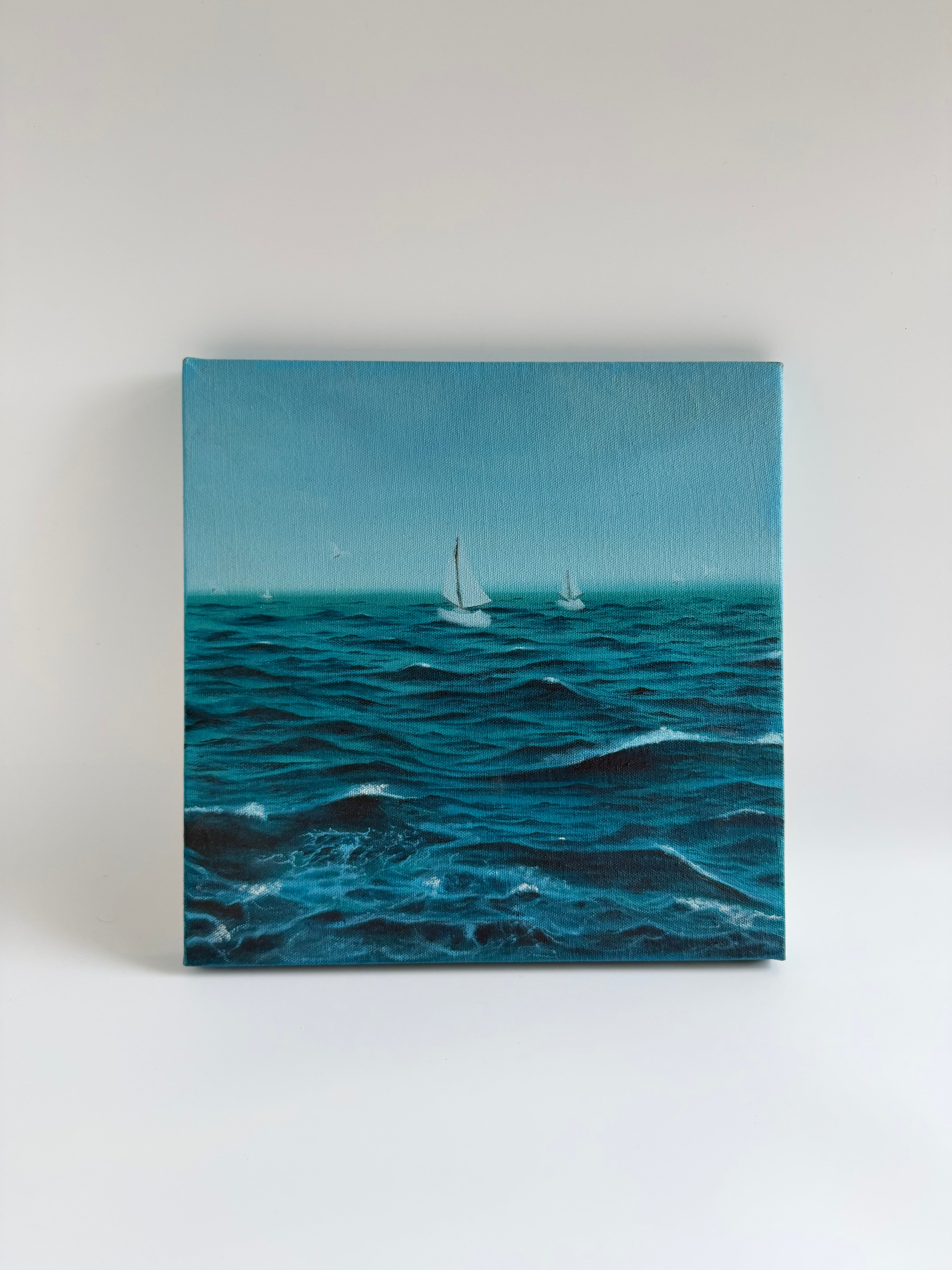 Original stormy sailboat oil painting featuring a lone sailing boat navigating dramatic ocean waves on a 12×12 square canvas by Shreya Chandra.