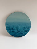 Original round ocean oil painting featuring calming blue waters on a circular stretched canvas.