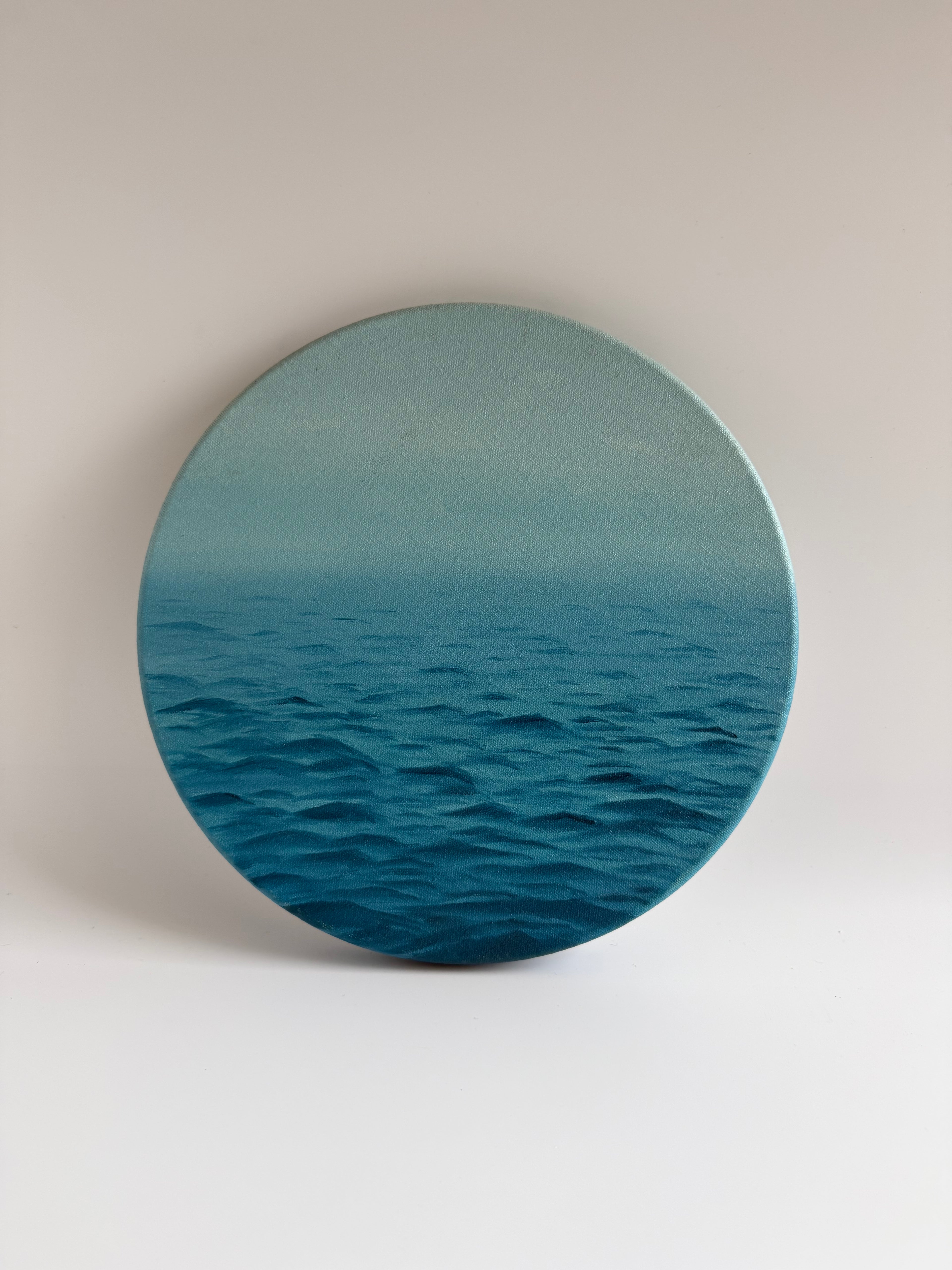 Original round ocean oil painting featuring calming blue waters on a circular stretched canvas.