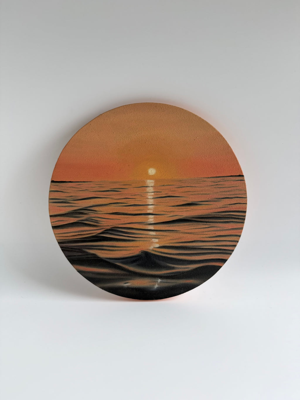 Original round ocean sunset oil painting featuring glowing golden reflections over calm coastal waters on a 12-inch round canvas by Shreya Chandra.